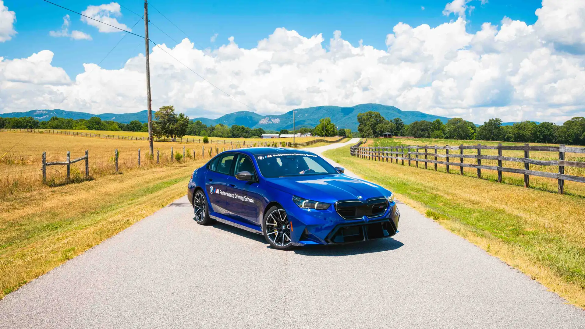 Blue BMW M5 on a country lane between fenced pastures