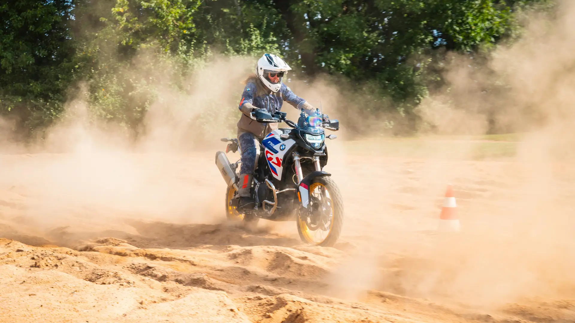 Rider powering a BMW F 900 GS through deep sand past a course cone
