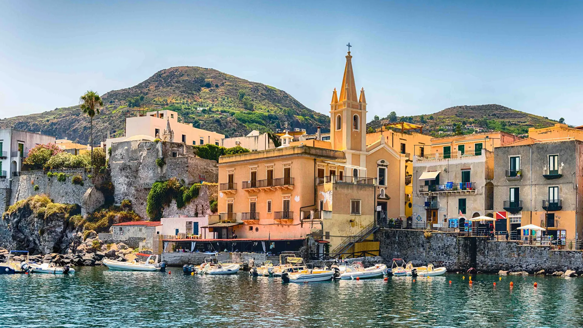 Sicilian harbour town with a bell tower above moored fishing boats
