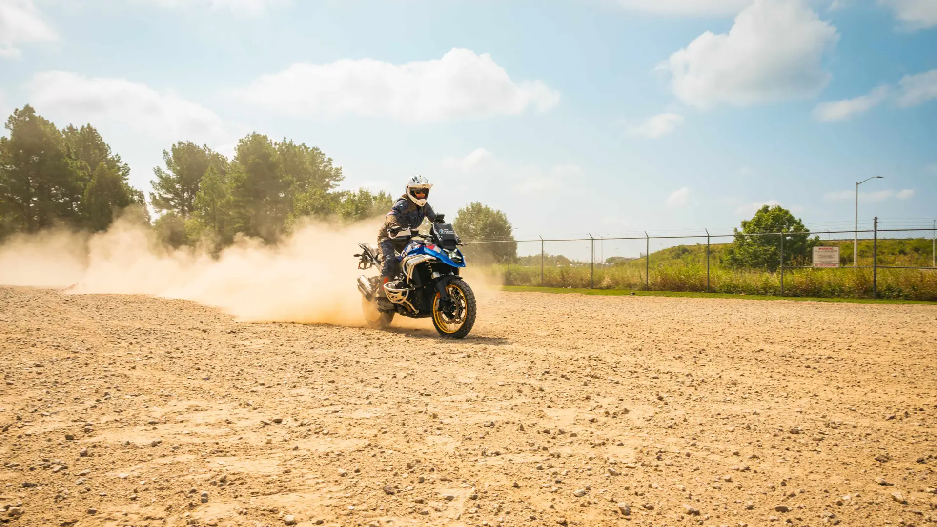 Rider sliding a BMW GS through loose gravel, throwing up a cloud of dust