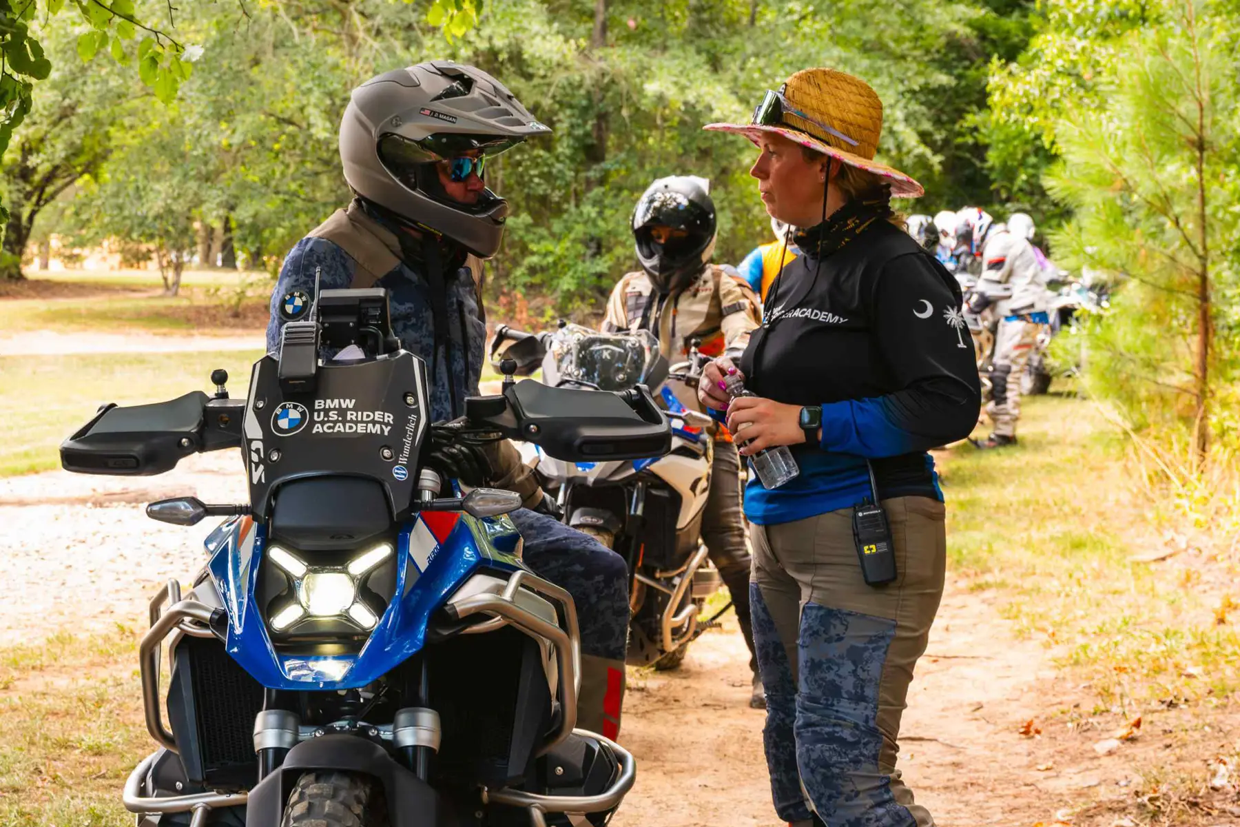Instructor talking with a rider beside a BMW GS on a wooded trail