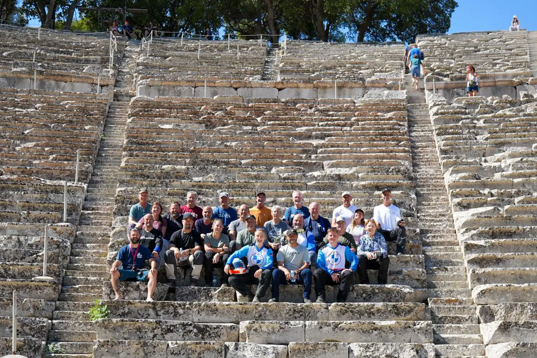 Tour group seated on the stone tiers of an ancient Greek amphitheatre