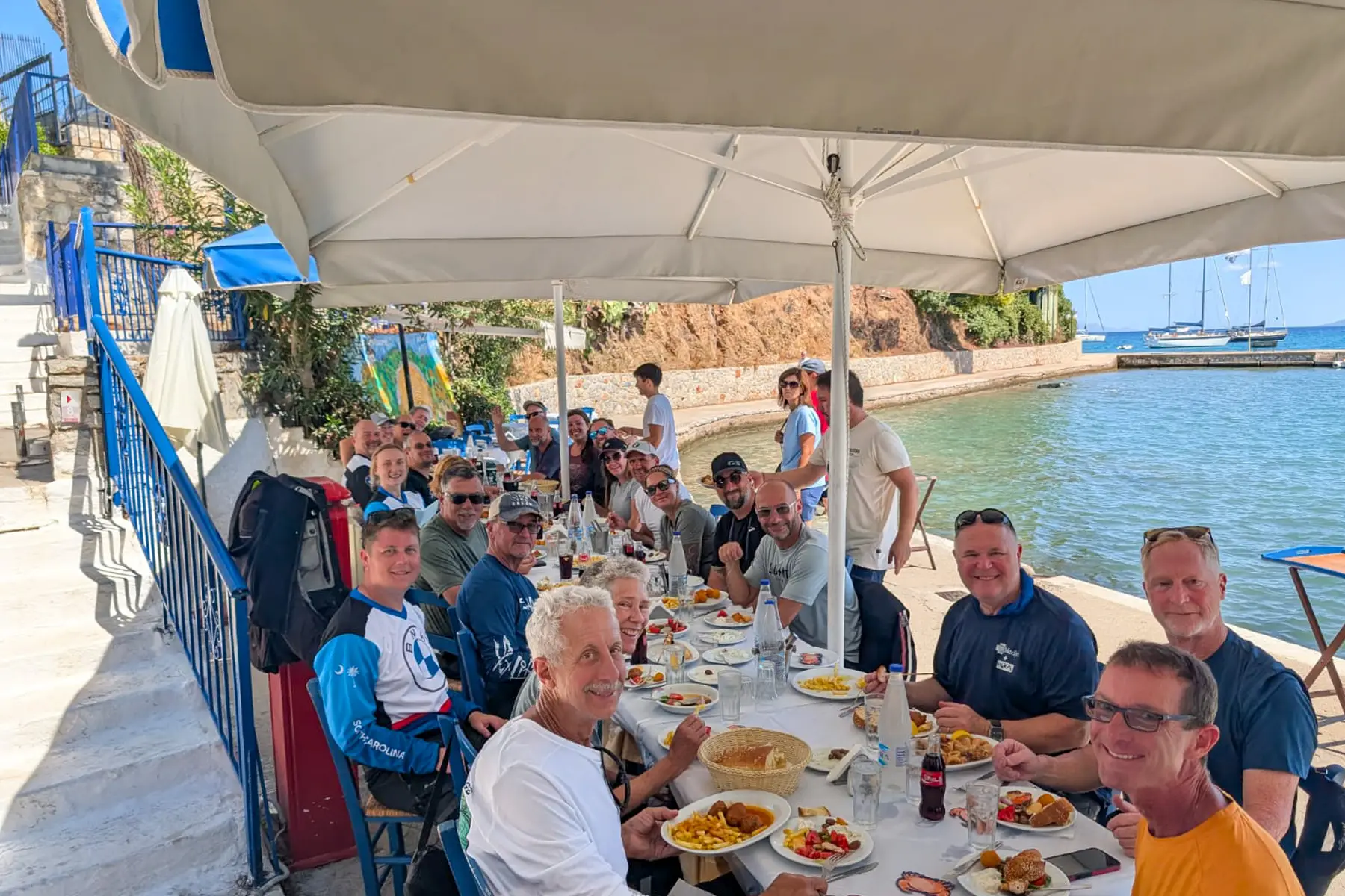 Tour group sharing a meal at a long table beside the water