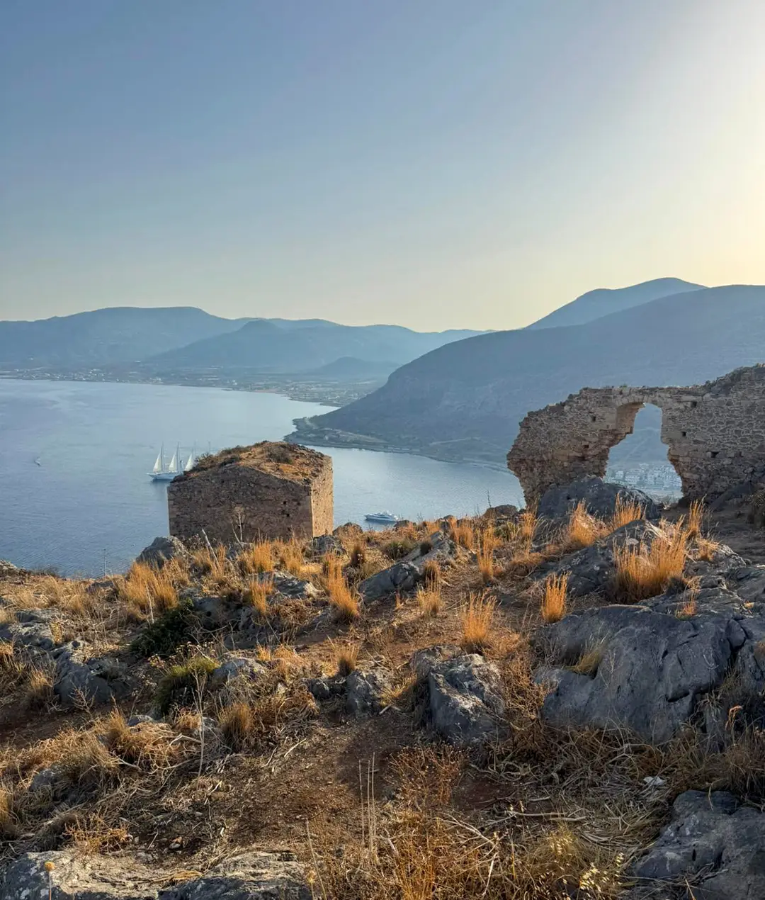 Stone ruins on a hillside above a Greek bay at golden hour