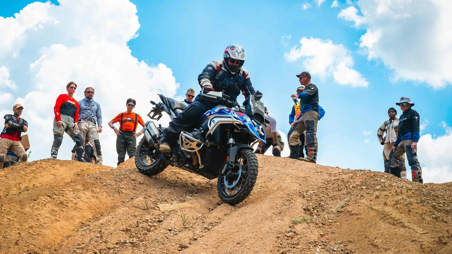 Rider cresting a dirt mound while classmates watch from the ridge