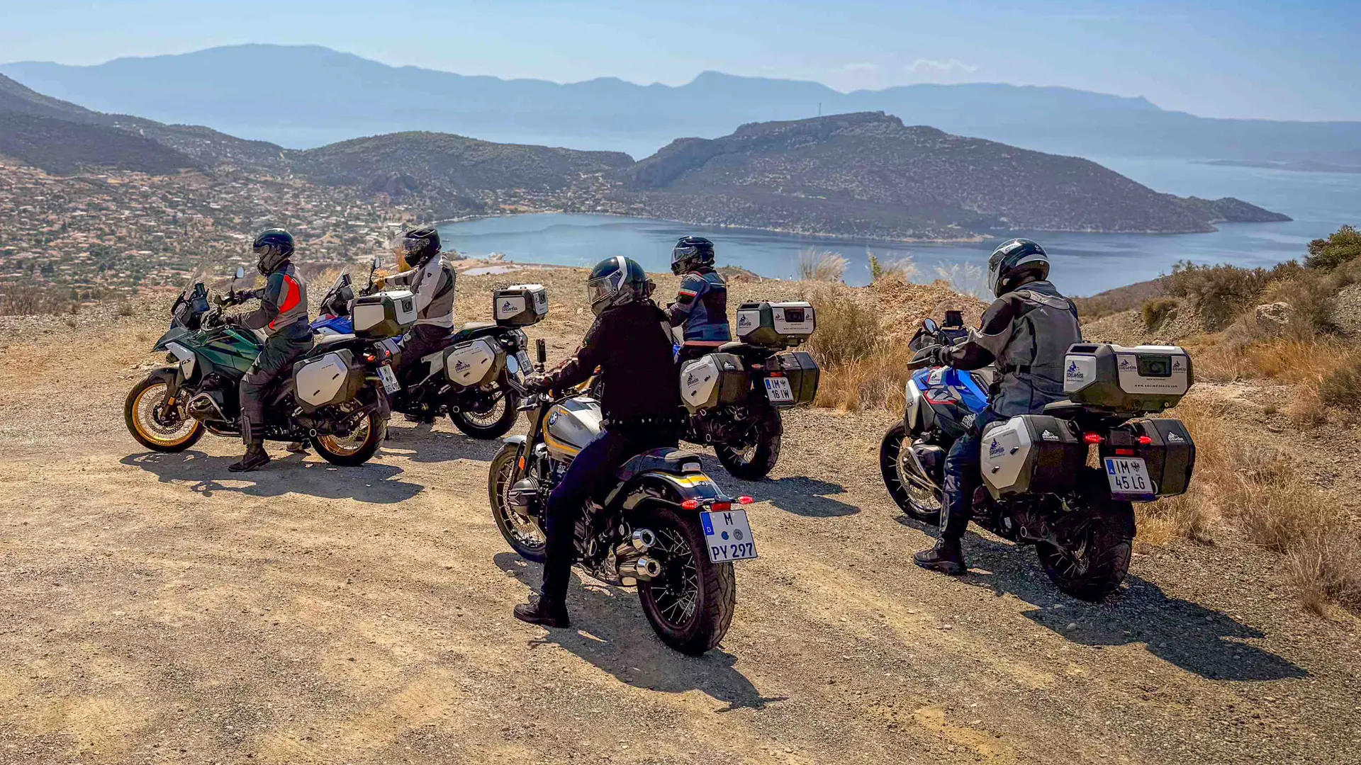 Riders on adventure motorcycles pausing at a gravel overlook above the coast