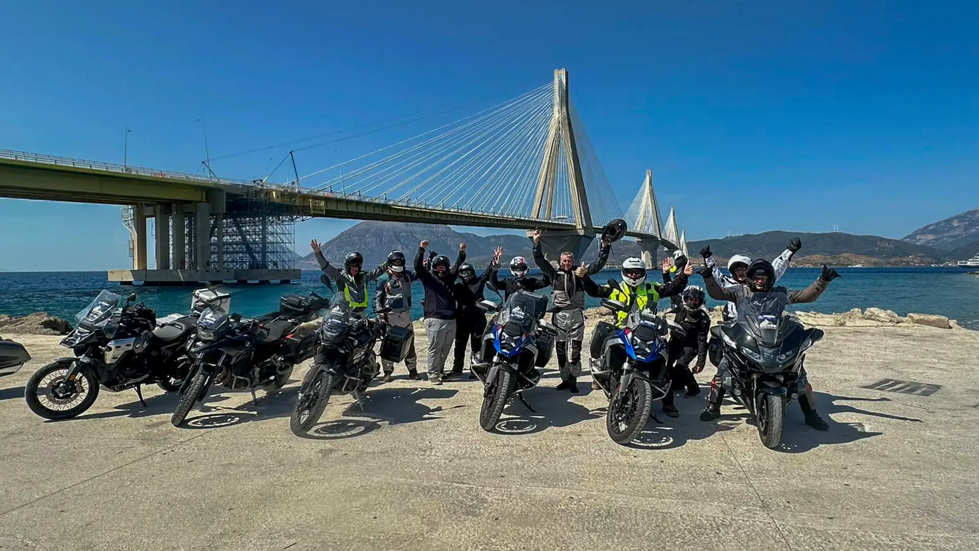 Tour group celebrating beside their motorcycles in front of a cable-stayed bridge