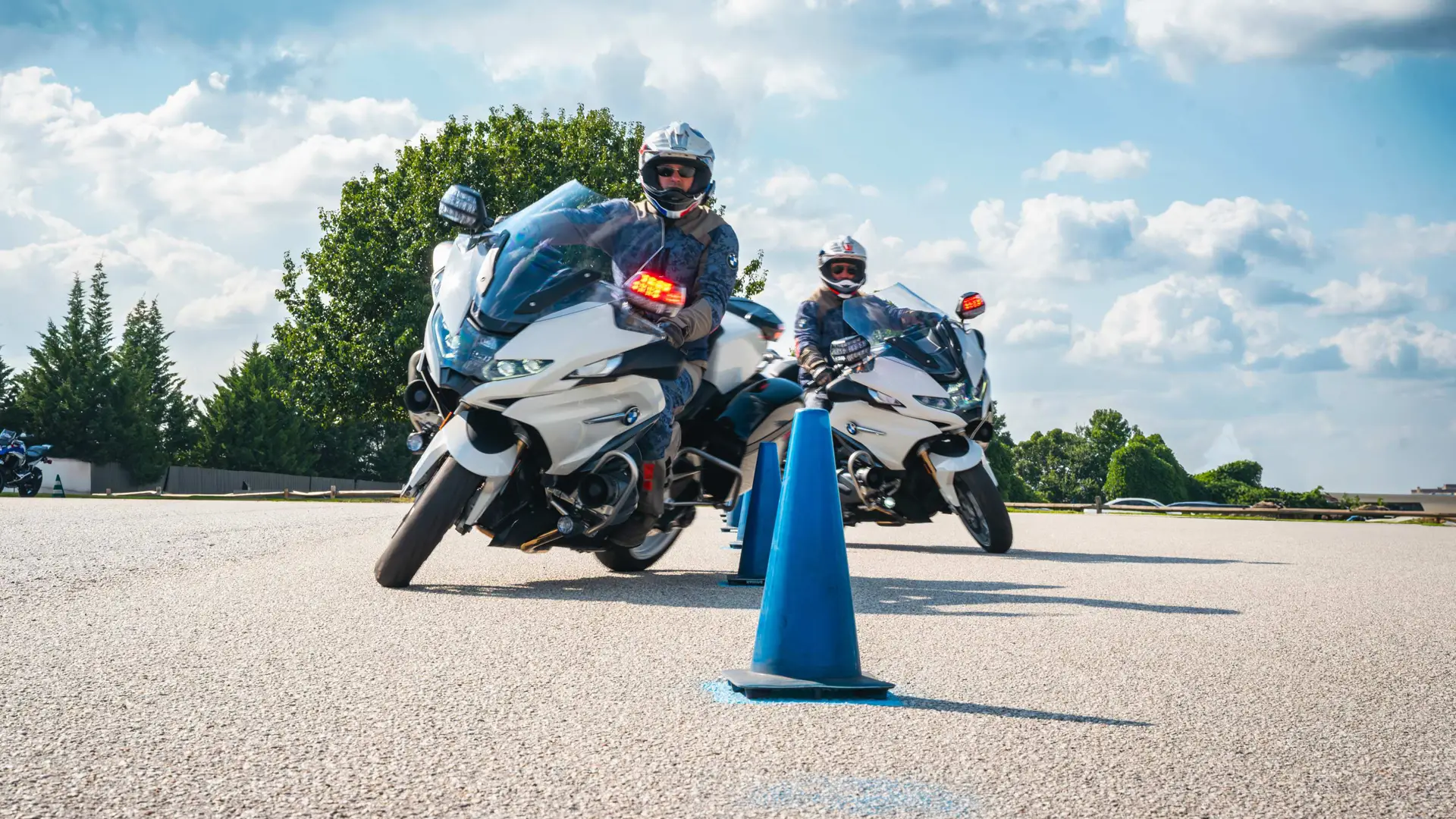 Two riders on white BMW police motorcycles beside a cone on the training pad