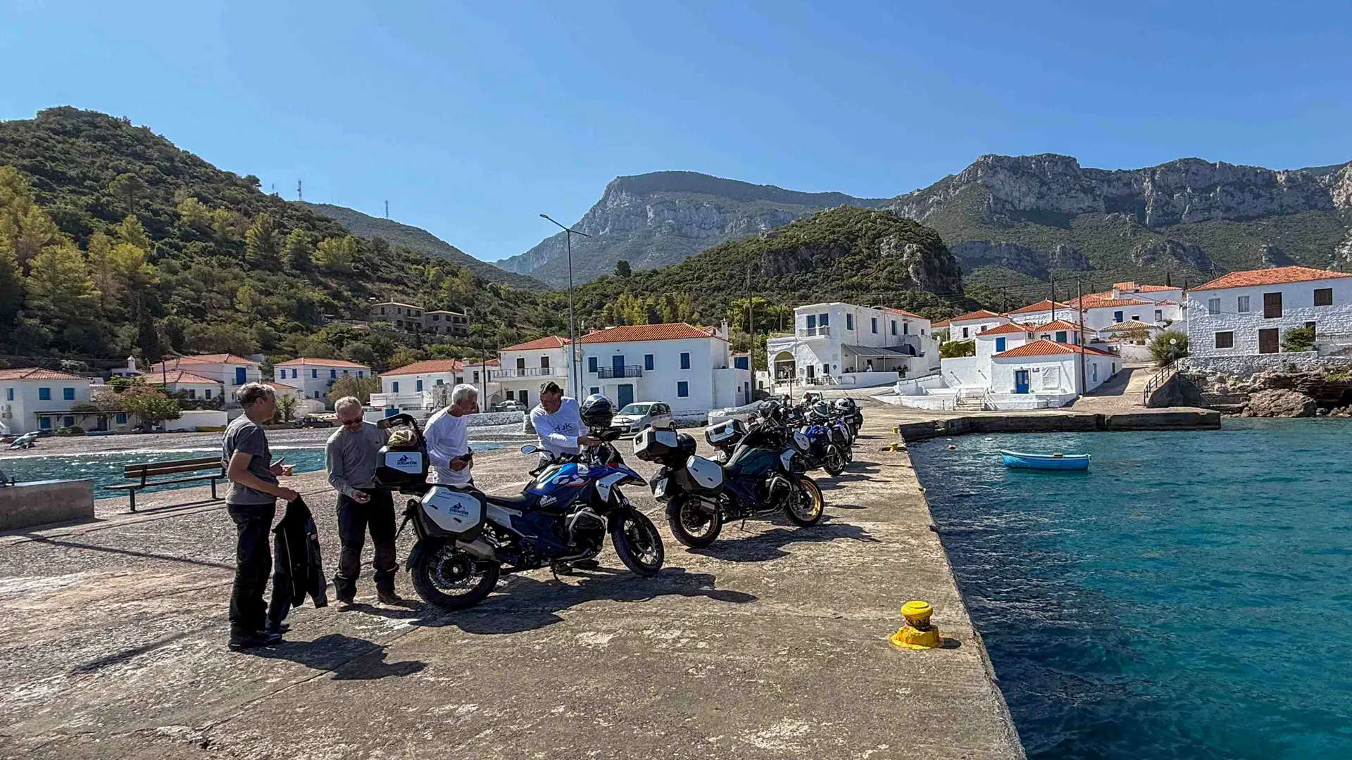 Riders and BMW GS motorcycles parked on a harbour quay in a Greek village