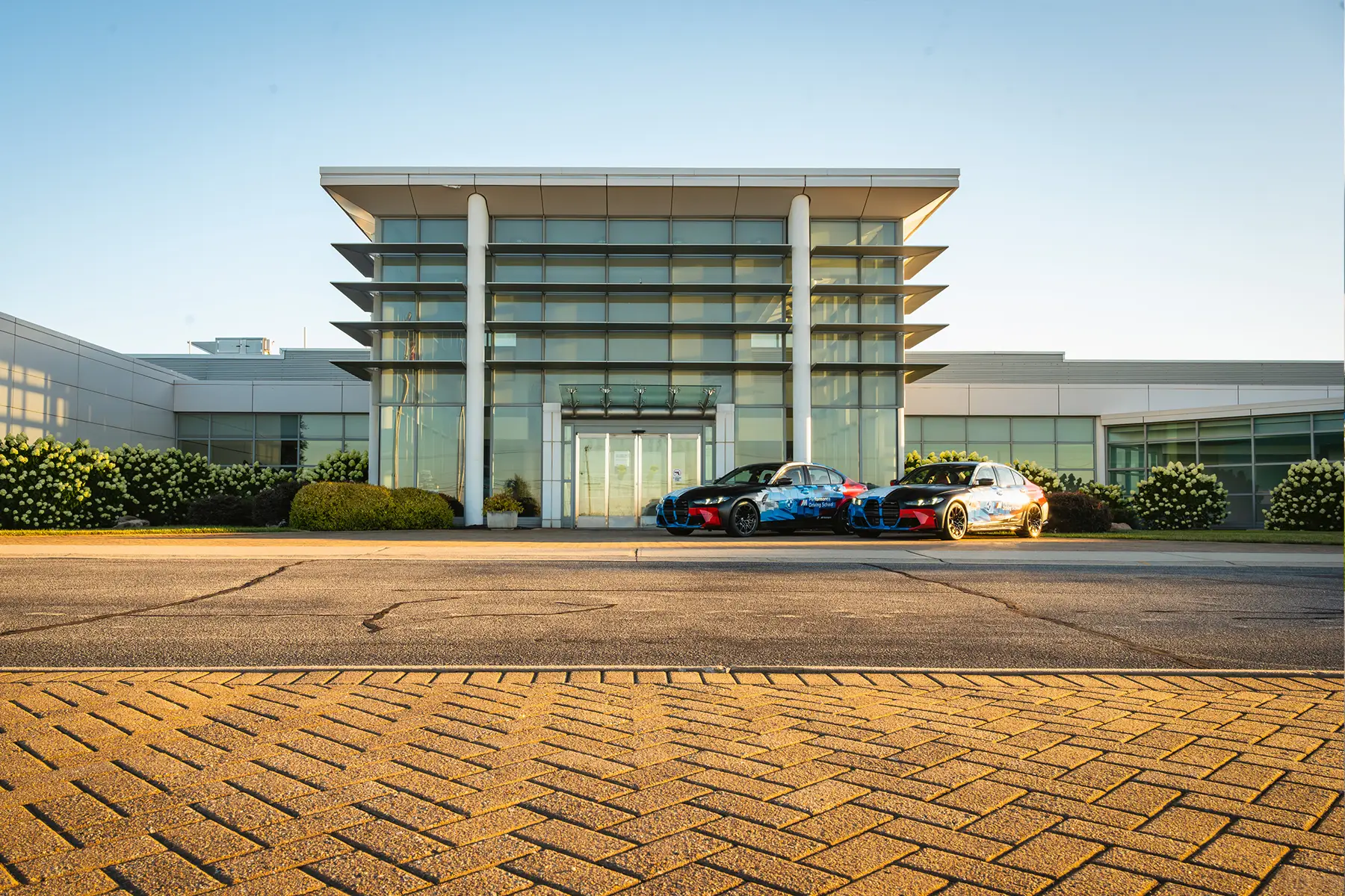 Two liveried BMW M cars parked outside the BMW Performance Center entrance